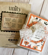 The Unity stamp packaging for the sentiment kit shown with a boxed set of finished floral cards and lace ribbon.