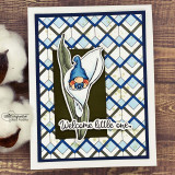 Sample card with the boy gnome in a blue hat tucked in a white calla lily on navy and light blue argyle, with 'Welcome little one'.