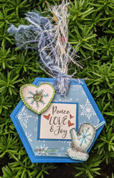 Blue hexagon ornament tag with 'Peace Love & Joy' hung on a pine tree.