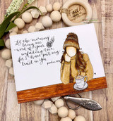 The girl in a golden coat cradling coffee on a wood-plank card with a handwritten script background.