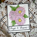 Soft pink asters with yellow centers on a white stitched card with a black 'hugs & kisses' banner on a doily.