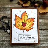 Orange and yellow maple leaf with a red heart on a white card with a brown mat, stamped 'In every thing give thanks'.