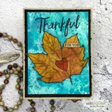 Two rust maple leaves with a red heart on a teal watercolor background with a black Thankful die cut.