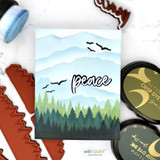 Card made with the Heart of Christmas dies — die-cut 'peace' over a blue mountain and pine landscape.