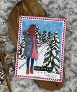 Card with the girl colored in blue and red against the snowy pine forest, framed in red polka dots on a wooden tray.