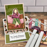 Layered card of the seated girl in a mauve top on floral papers, 'the simple pleasures are life's greatest treasures.'
