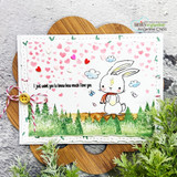 Whimsical card with a bunny and floating hearts over a grassy layered scene.