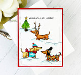 Red-framed card with three dachshunds in holiday gear trotting through snow under 'Wishing you a jolly holiday'