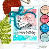 Pink to teal watercolor card with a white clock face, roses, a fuzzy teal bow and 'Happy Birthday', shown with Magical pigment jars