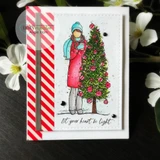 A nesting-die frame around a girl with a Christmas tree, 'let your heart be light.'