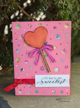 A coral heart lollipop with a pink bow on a pink star-print card, reading 'You're the Sweetest.'