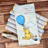 Blue balloon Pooh card with die-cut clouds displayed on a fan of gray Copic markers.
