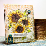 Card of three colored sunflowers stamped over a lace-textured cream panel with 'Sending love & prayers' on a banner.