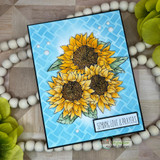 Sunflower cluster colored and mounted on a soft blue textured background with white beads alongside.