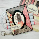 Card sample — a girl holding coffee, 'you light up the world just by being you', on XOXO love-script Enveloped in Love paper.