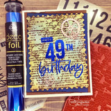 Navy layered card beside a tube of blue transfer foil, the map background stamped in gold on tan, with a foiled birthday number layered on top.