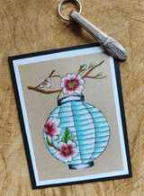 Kraft card with the paper lantern colored bright blue and the cherry blossoms in pink, framed in black and white, with a Unity spatula tool beside it.