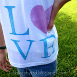 White T-shirt stamped with LOVE in large letters, the L, V and E in blue and the heart in glittery purple.
