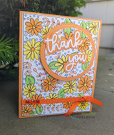 Card photographed outdoors with the daisy background coloured in orange, yellow and blue, an orange circle and a white 'thank you' die cut with orange ribbon.