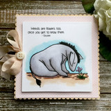 Eeyore sniffing a small flower on a soft scalloped card, 'weeds are flowers too, once you get to know them'.