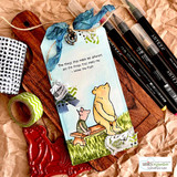 Kraft gift tag with watercolored Pooh and Piglet on a bench, the 'things that make me different' Winnie the Pooh sentiment and a blue ribbon.