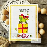 White card with the gnome in a green hat on yellow and red presents, stamped ''tis the season to be JOLLY' and dotted with green sequins.