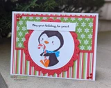 Christmas card with a penguin in a blue scarf holding a candy cane on a red scalloped circle over green and red snowflake and stripe papers, 'May your holidays be sweet'