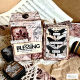 Tags in pink and cream stamped with the butterfly panel, a "find the BLESSING in everything" strip, and small word tags, over sheet music and kraft paper.