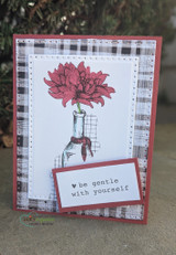 Black plaid card with the bloom in deep red in a grey bottle and 'be gentle with yourself' on a white tag.