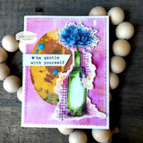 Card with a gold and pink blended circle behind the bloom in blue and a green bottle, with 'be gentle with yourself' on a black strip.