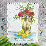 Yellow rain boots holding red roses under stamped raindrops with a blue watercolor puddle and the sentiment 'When life throws you a rainy day, play in the puddles'