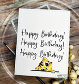White card with 'Happy Birthday!' stamped three times and a yellow tabby peeking up from the bottom edge.