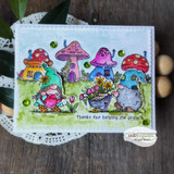 Handmade card made with Unity Stamp Co’s Garden Gnomes red rubber stamp set — garden gnomes — one pushing a flower cart, one watering blooms — with a hedgehog helper — stamped and colored, with the sentiment “Plant smiles”.