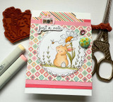 Card with the bunny and daisy in a circle over diamond paper with a rubber stamp alongside.