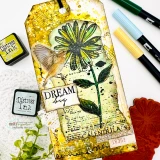 Handmade card made with Unity Stamp Co’s Joy In Your Dreams red rubber stamp set — a tall calendula flower with a botanical label, a butterfly and mixed-media text collage — stamped and colored, with the sentiment “Dream big”.