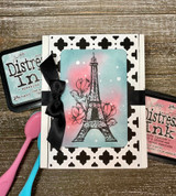 Distressed black-and-white card of the Eiffel Tower with pink and blue accents.