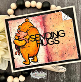 Card with Pooh hugging Piglet over a warm inked background and 'SENDING HUGS.'