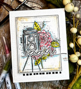 White embossed card with the camera and roses in pink and yellow tones above a black film-strip border, with a die-cut word from another set.