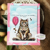 Pink-framed birthday card of the tabby with a pink balloon on a cloud background.