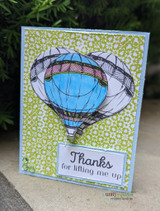 Olive green tile pattern card with a hand colored blue and pink hot air balloon and a label reading thanks for lifting me up.