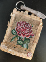 Mixed media sample tag with the dictionary rose colored soft pink on a torn and crackled cream panel, finished with a small number tag and a metal ring.