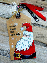 Kraft tag with red and white ribbons: Santa in a red hat and blue coat beside “HE KNOWS if you've been BAD OR GOOD.”