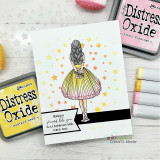 Soft card with the girl in a yellow skirt over a pale star-dotted background beside Distress ink pads.