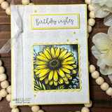 Card with a yellow daisy over embossed white and 'Birthday wishes.'
