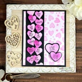 Cream embossed card with a black and pink striped panel, a column of pink hearts each stamped with a short word and a larger love heart at the bottom, styled with wooden heart and key accents.