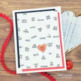 Navy framed card with the full word grid stamped in black on white, one pink heart coloured in the centre, red enamel dots and a red pom trim.