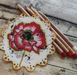 Card of the pink poppy on a scalloped kraft frame with pencils alongside.