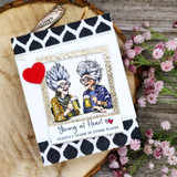 Card with the two grannies in a burlap frame over black heart-print paper, 'Young at Heart ... slightly older in other places.'