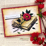 Card with an open book and a rose over script paper, 'What is remembered, lives'