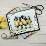 Card with the colored hens layered on patterned papers, coloring markers and scissors beside it